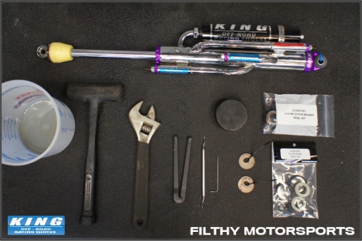 Photo of shock servicing tools: hammer, spanner wrench, pick, allen wrenches, bucket, and hockey puck