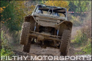 A photo of a black vehicle driving down a dirt road with front tires in the air with ORI struts