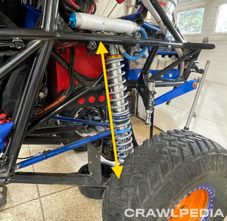 A photo of the rear corner of a rock crawler with a King coilover and an arrow showing the distance between mounts